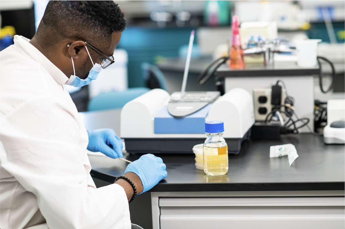 student at a lab counter wearing a white lab coat