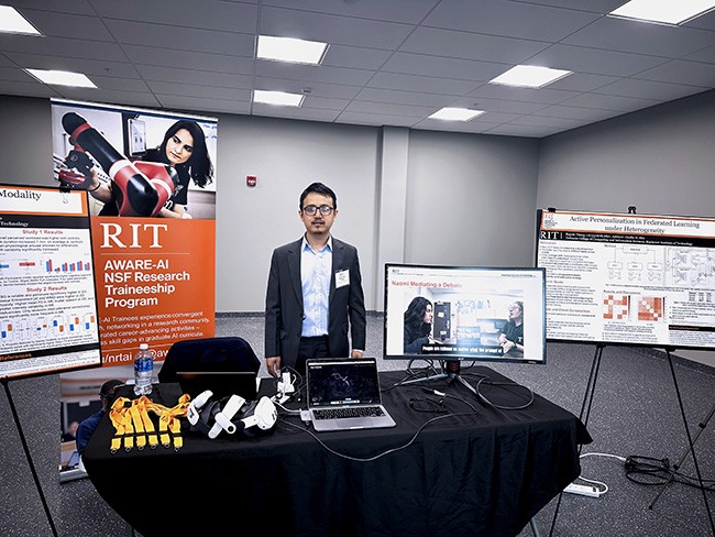 Trainee Rajesh Titung stands at a table displaying a laptop, monitor, and peripheral devices related to research