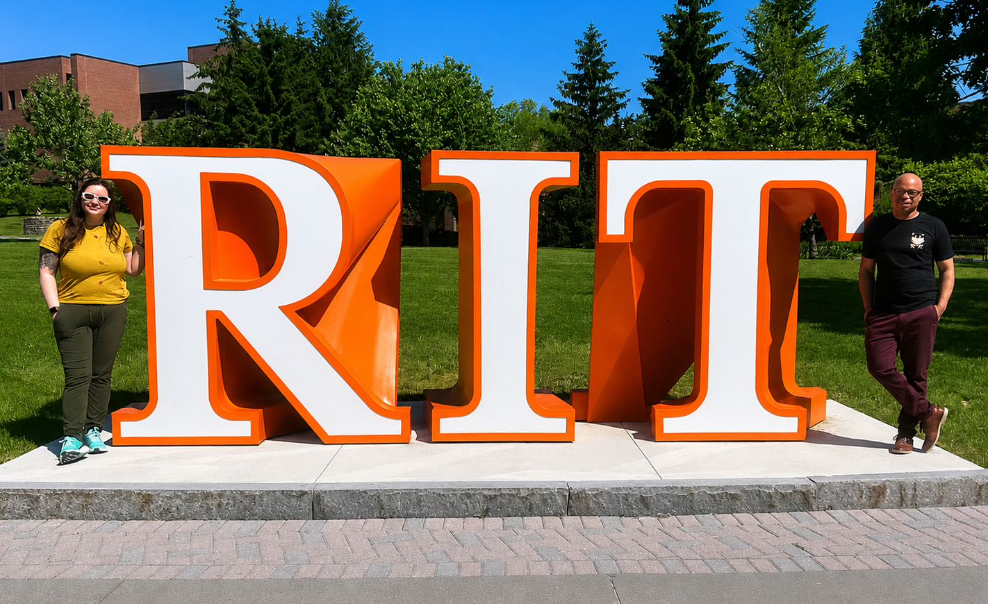 Universal AI trainees Paige DeVries and Joe Merino stand on either side of a large outdoor sign spelling out RIT on a sunny day