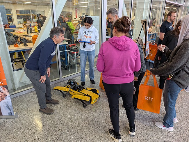 Visitors gather around a yellow quadruped Spot robot outside another robotics demonstration in a campus innovation space.