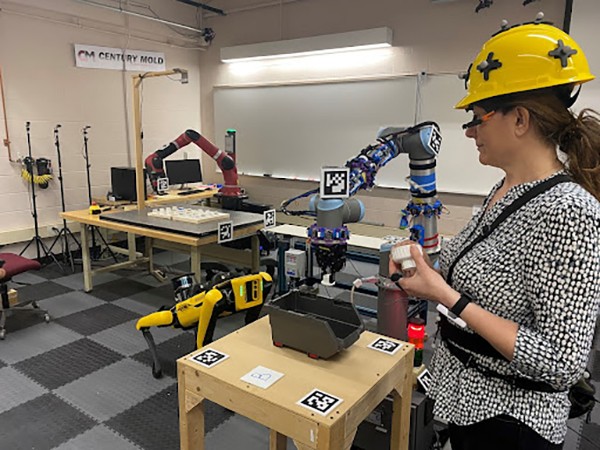 A participant is working with two industrial collaborative robots and a mobile robot.
