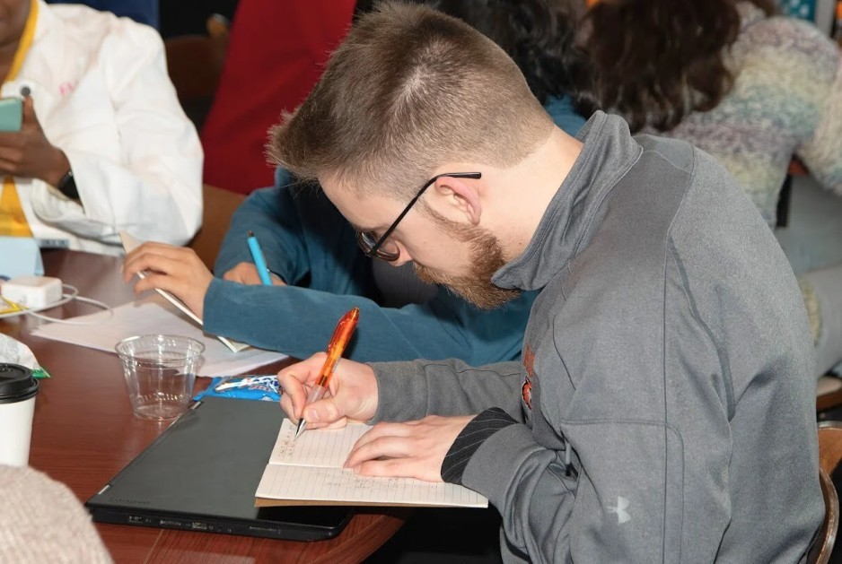 Student writing in a journal at a table during a writing retreat event