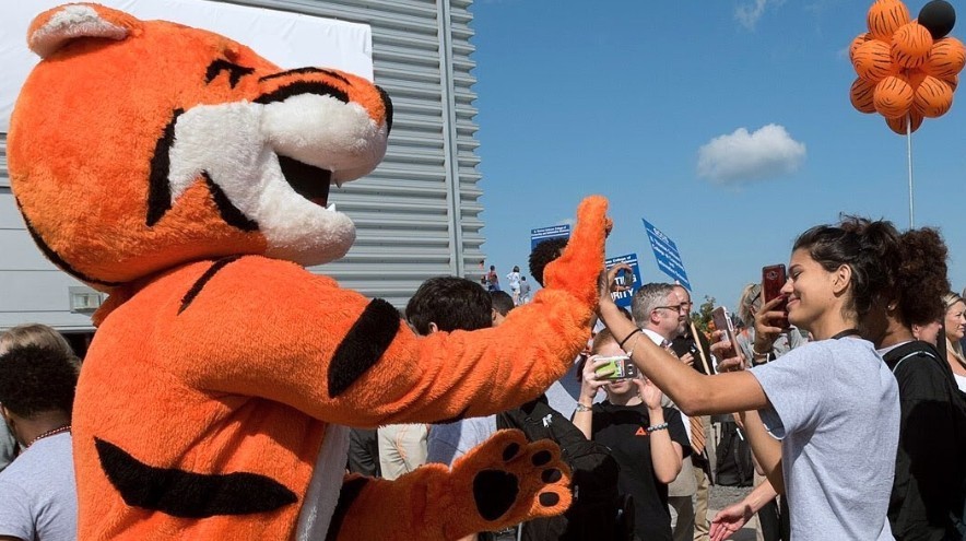 student give a high 5 to Ritchie, the RIT mascot with a crowd in the background at an orientation event