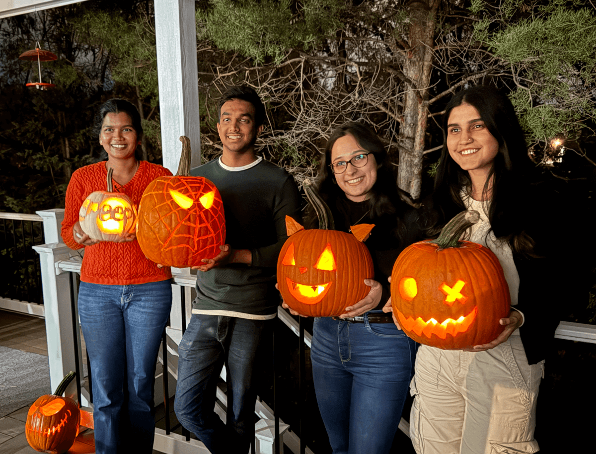 Four grad students with carved pumpkins lit from within, each featuring different designs including faces.