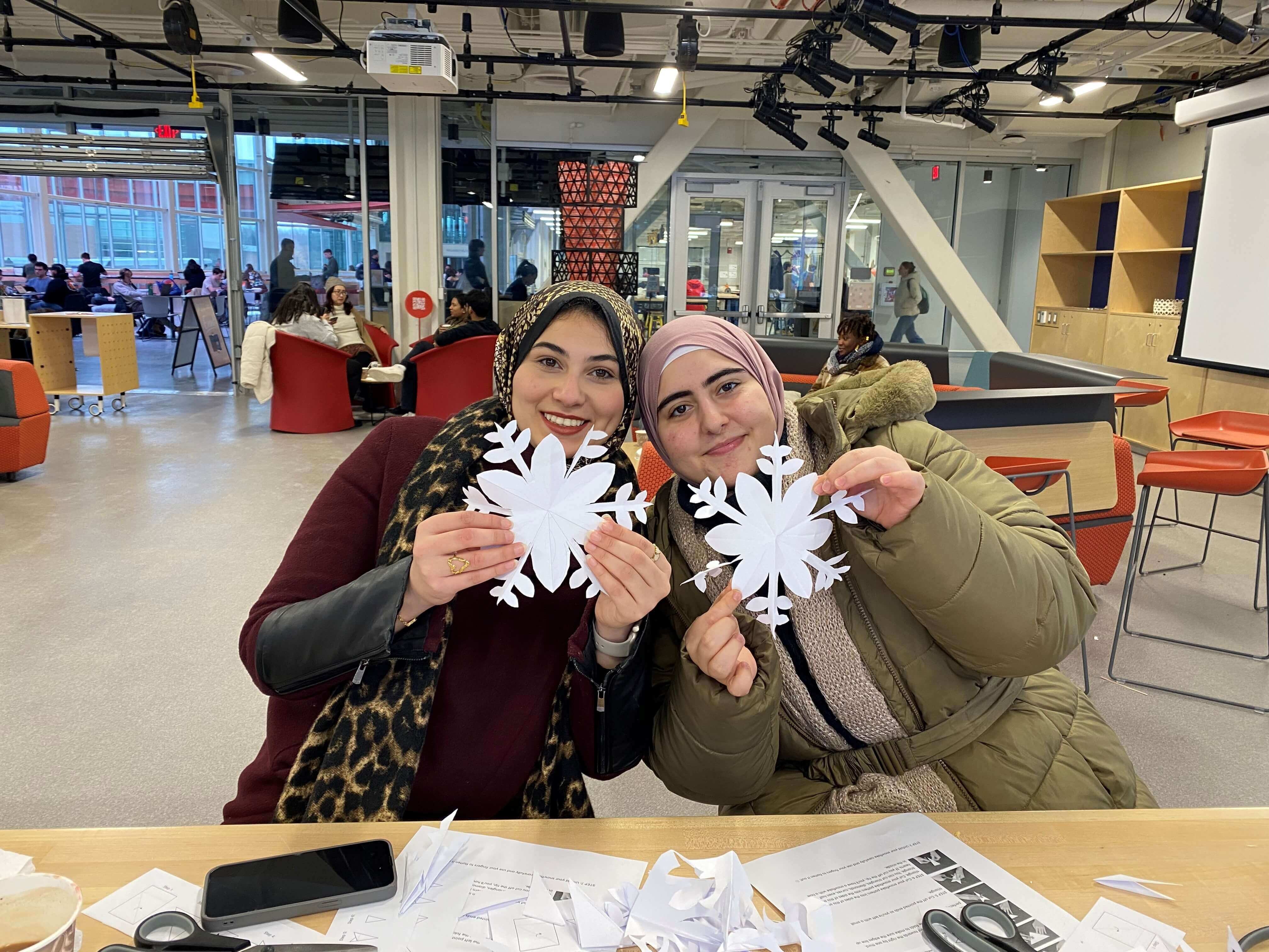 New graduate students sitting on a circular table with one student holding up and showing a gray RIT T-shirt while others smile at the camera