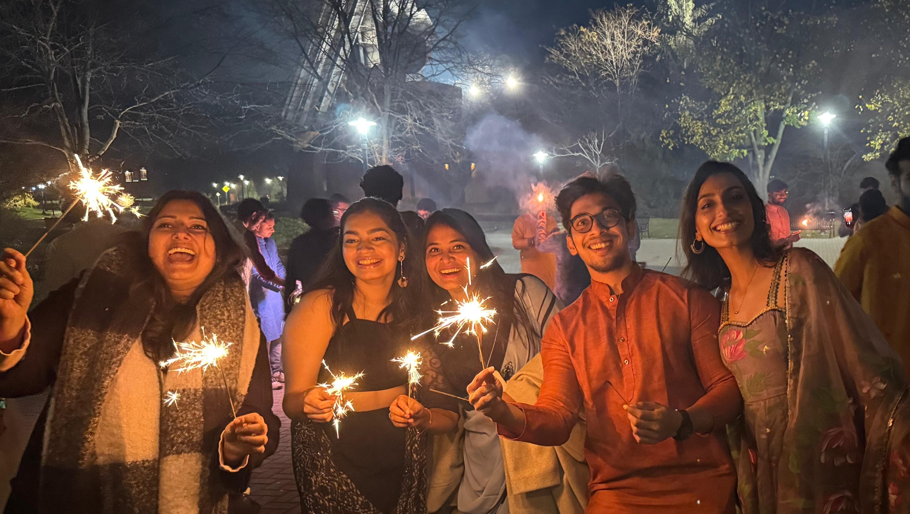 students pose holding bright sparklers at night