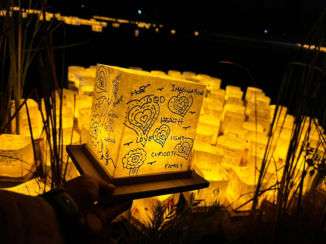 New graduate students sitting on a circular table with one student holding up and showing a gray RIT T-shirt while others smile at the camera