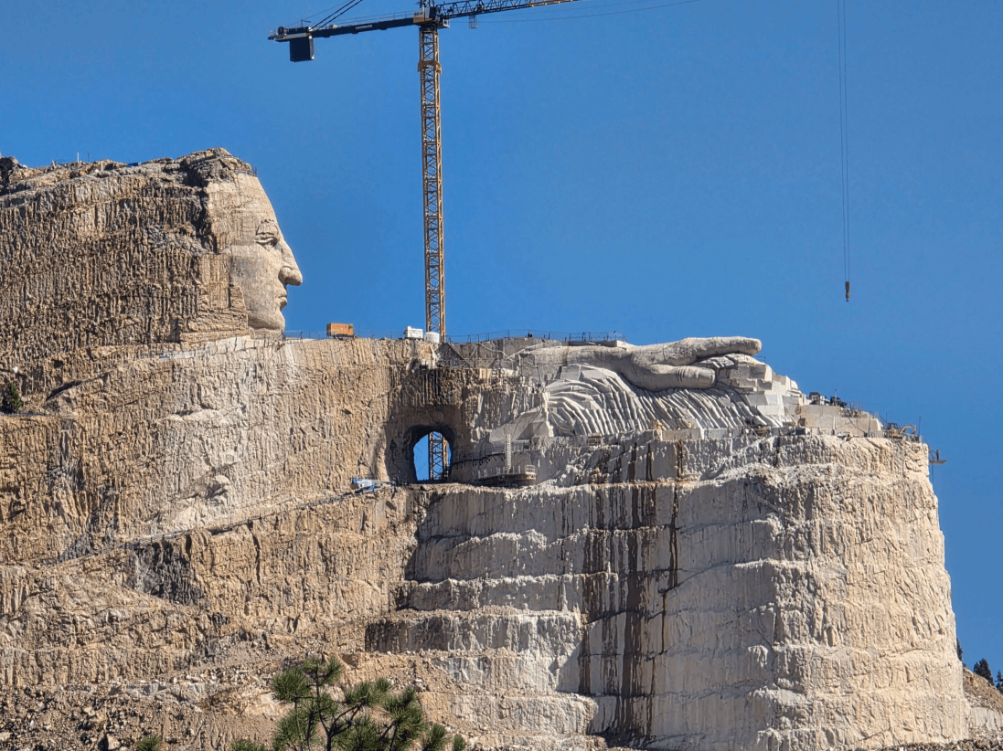 Rock-carved Crazy Horse Memorial with a crane above the unfinished sculpture.