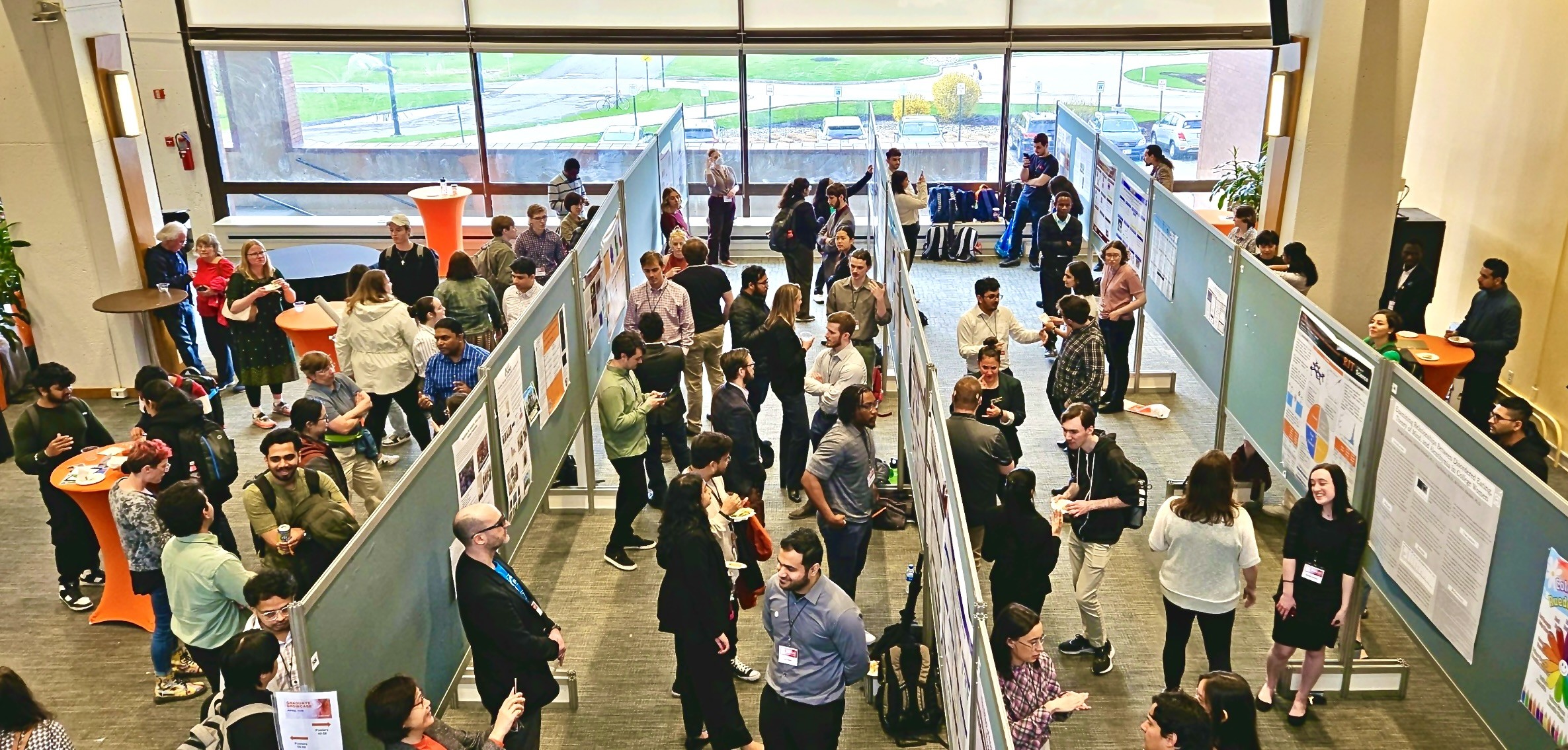New graduate students sitting on a circular table with one student holding up and showing a gray RIT T-shirt while others smile at the camera