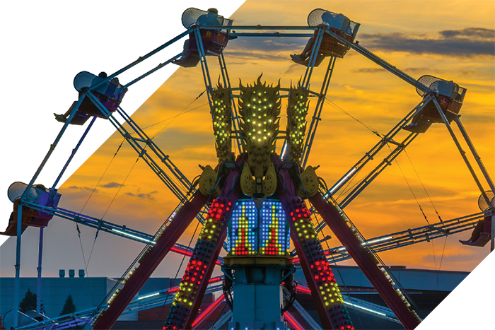 A lit carnival ride spins against a bright sunset sky with orange and yellow tones.