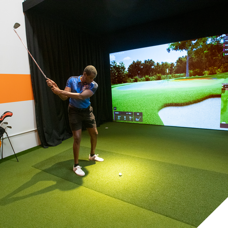 Person practicing a golf swing in an indoor simulator space.
