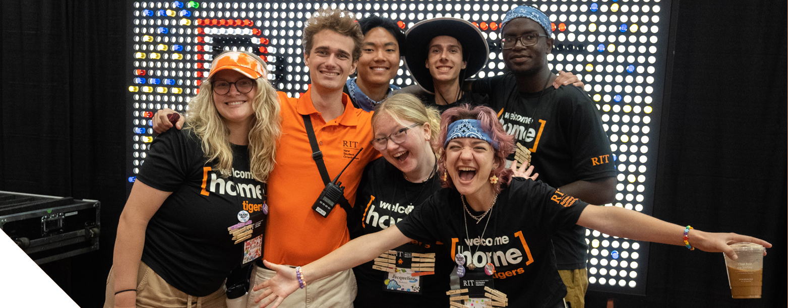 Group wearing black “Welcome Home Tigers” shirts posing together in front of a lit backdrop of circular lights.