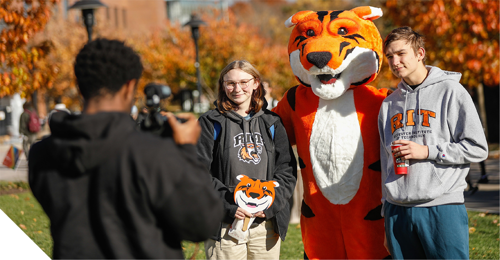 Two students pose for a photo with Ritchie's mascot on a sunny fall day on campus.