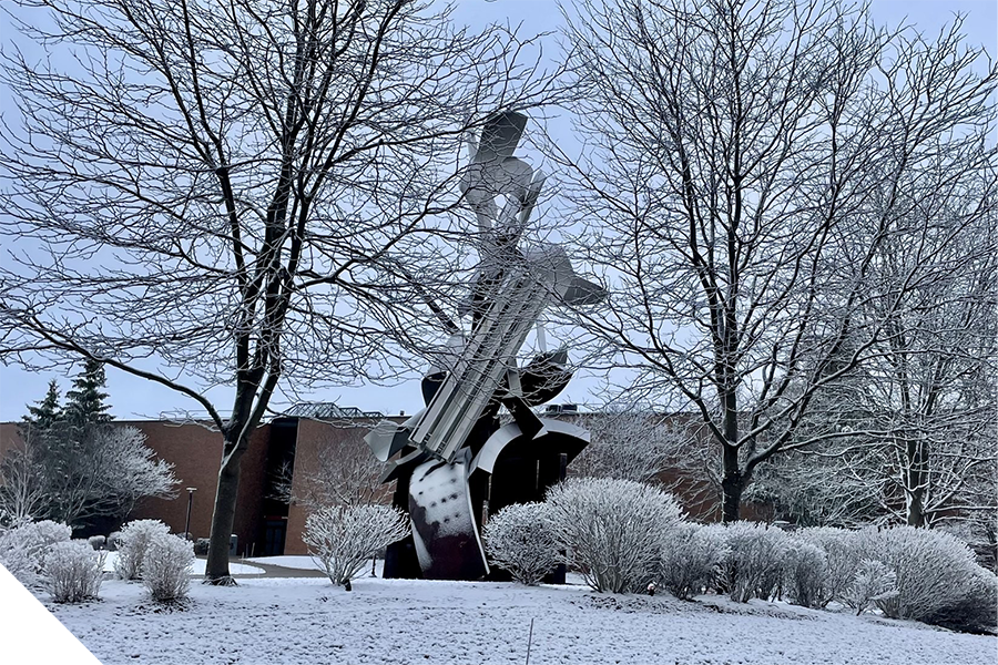 The Sentinel sculpture stands among snow-covered trees and bushes during winter on the RIT campus.