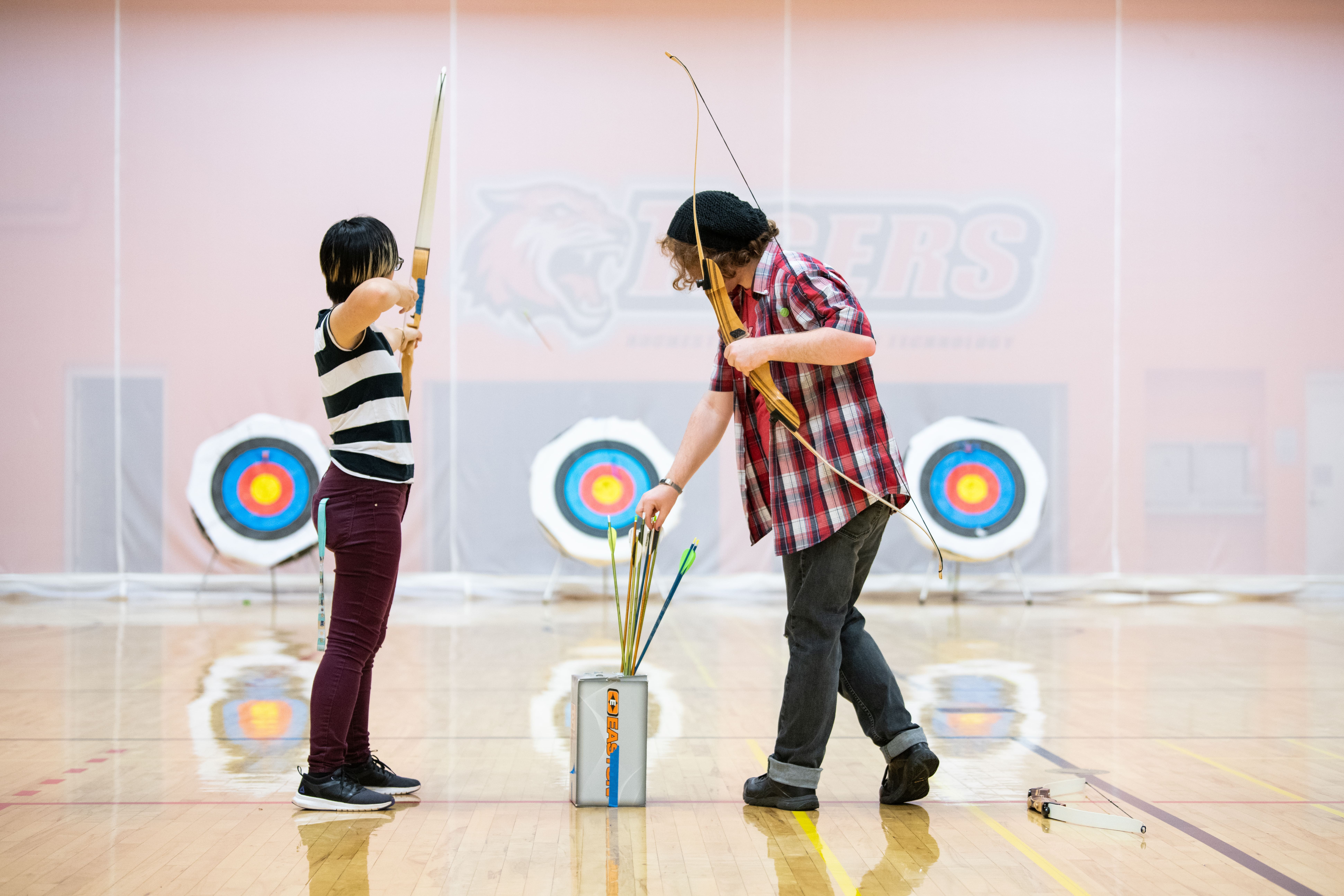 Two students playing archery in gym