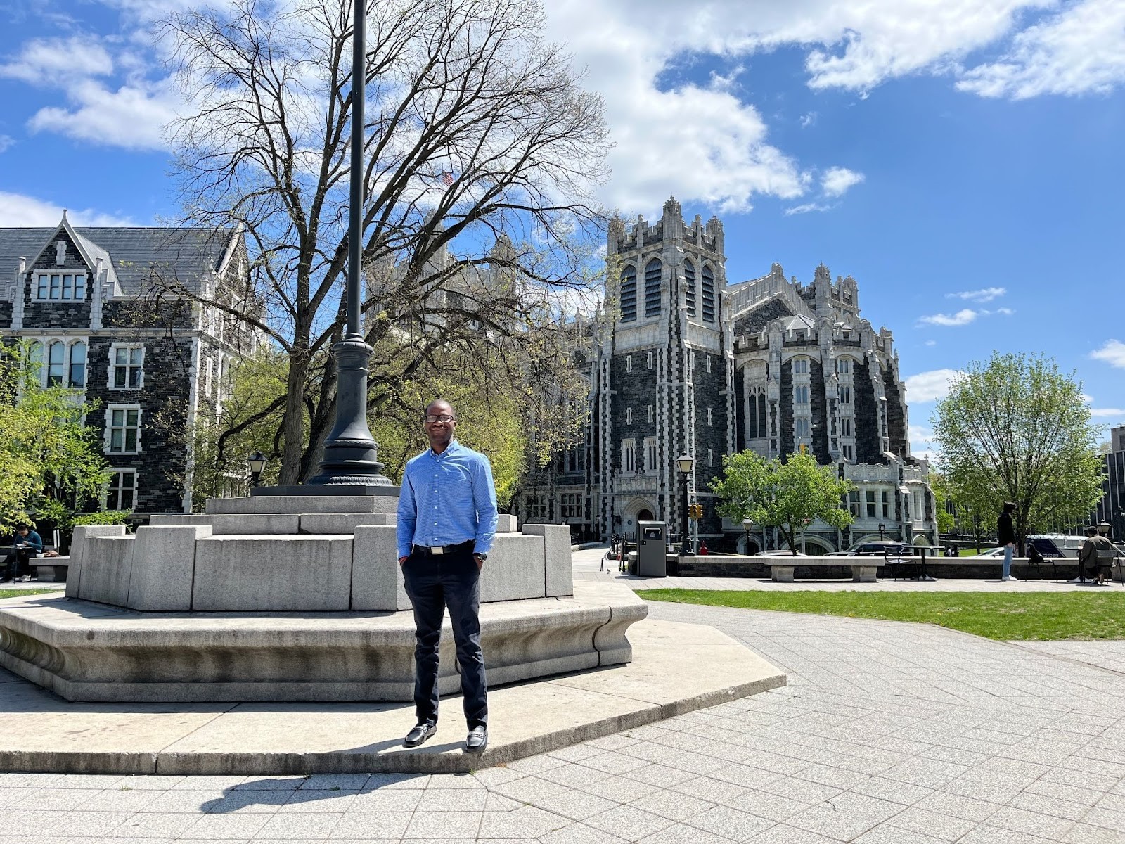 Justin Namba stands in front of campus buildings at CUNY on a sunny day.