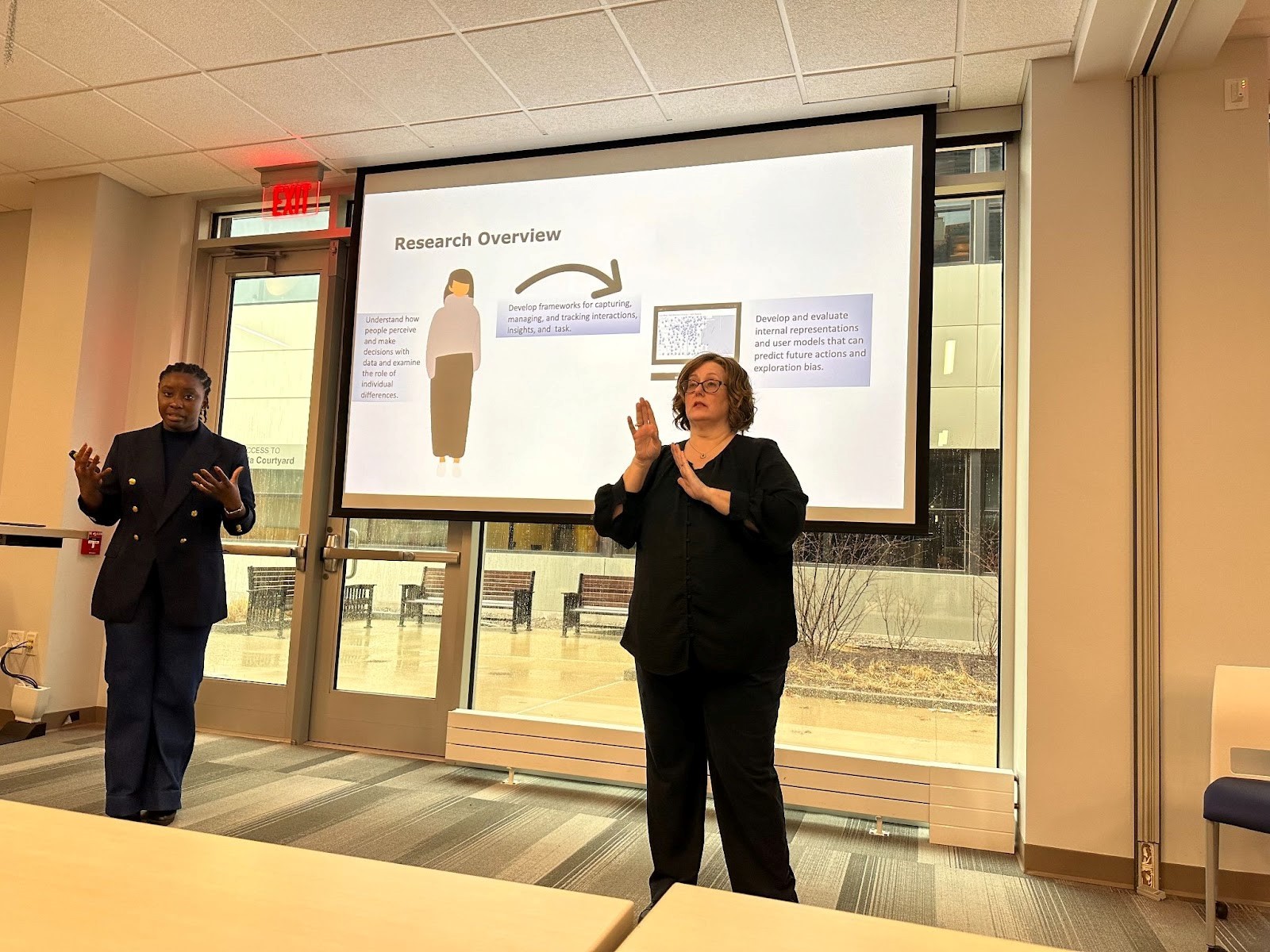 Alvitta Ottley stands during her presentation. Her slides, to the right of her, show a person with an arrow pointing to text. To the right of the slides is an ASL interpreter.