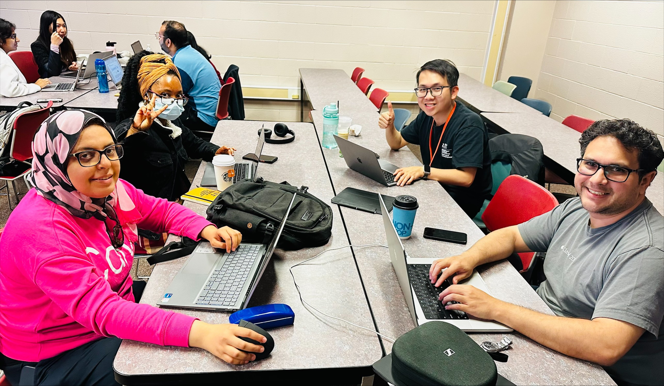 Four students sit around a table with laptops open in front of them, they face the camera and smile.