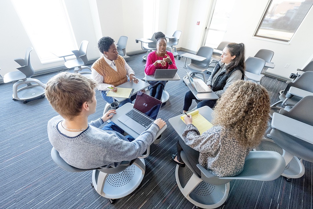 Group of 5 people sitting in a circle in a meeting space.