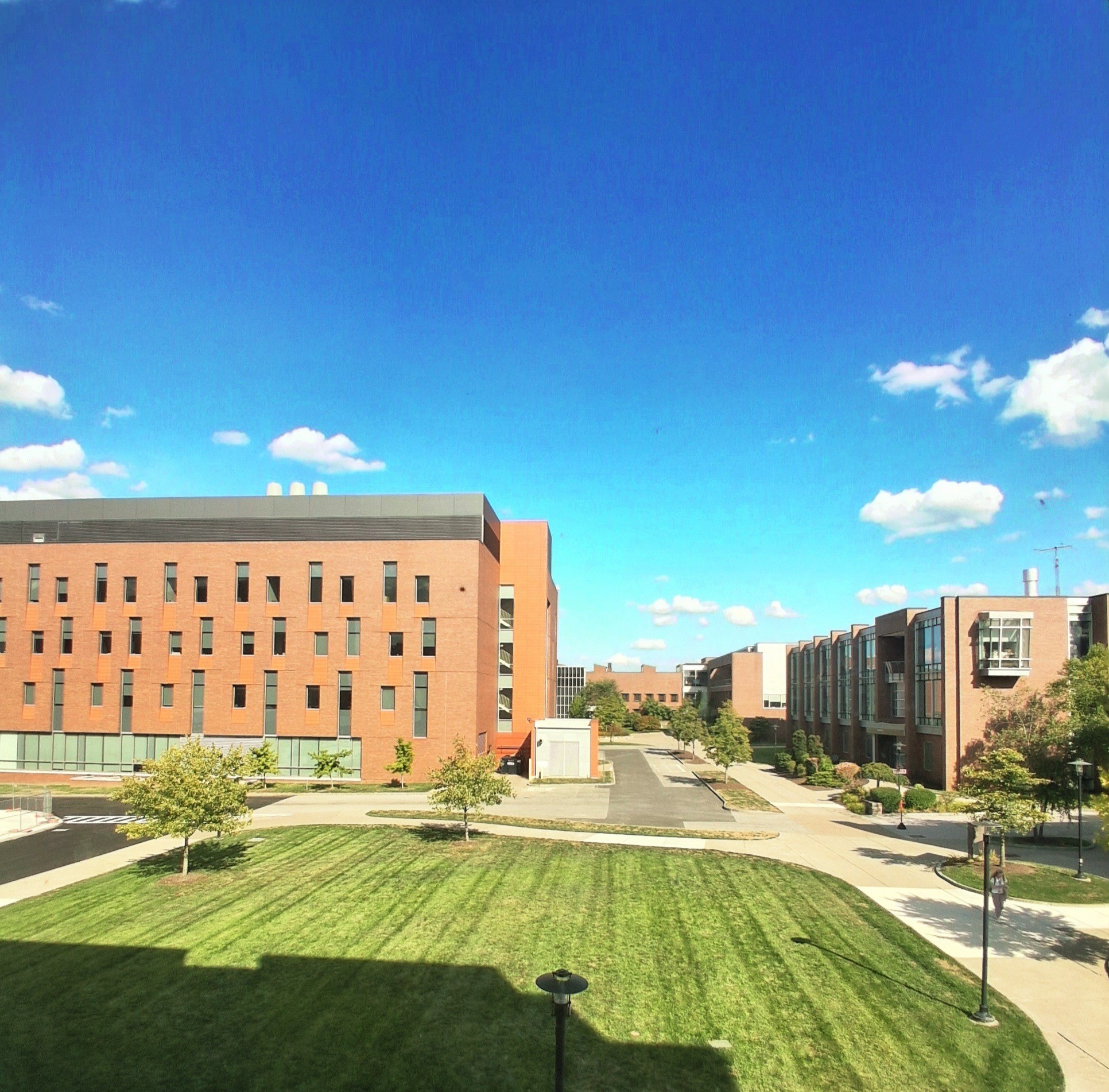 RIT campus with red-brick buildings, green lawn, and clear blue sky with scattered clouds.