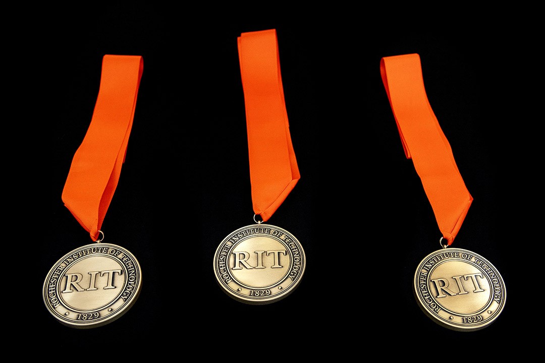 Three RIT medals with orange ribbons displayed against a black background.