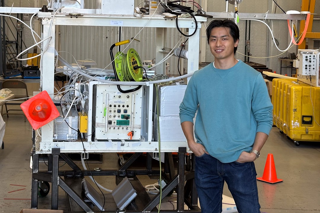 Person in a teal sweater standing beside technical equipment in a workshop.