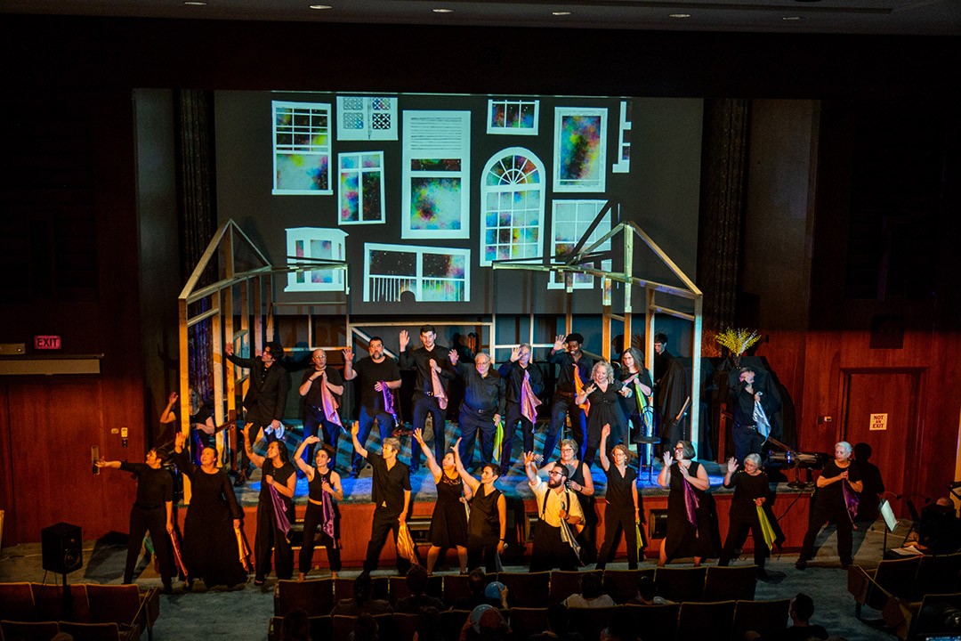 Group performing on stage with window projections.