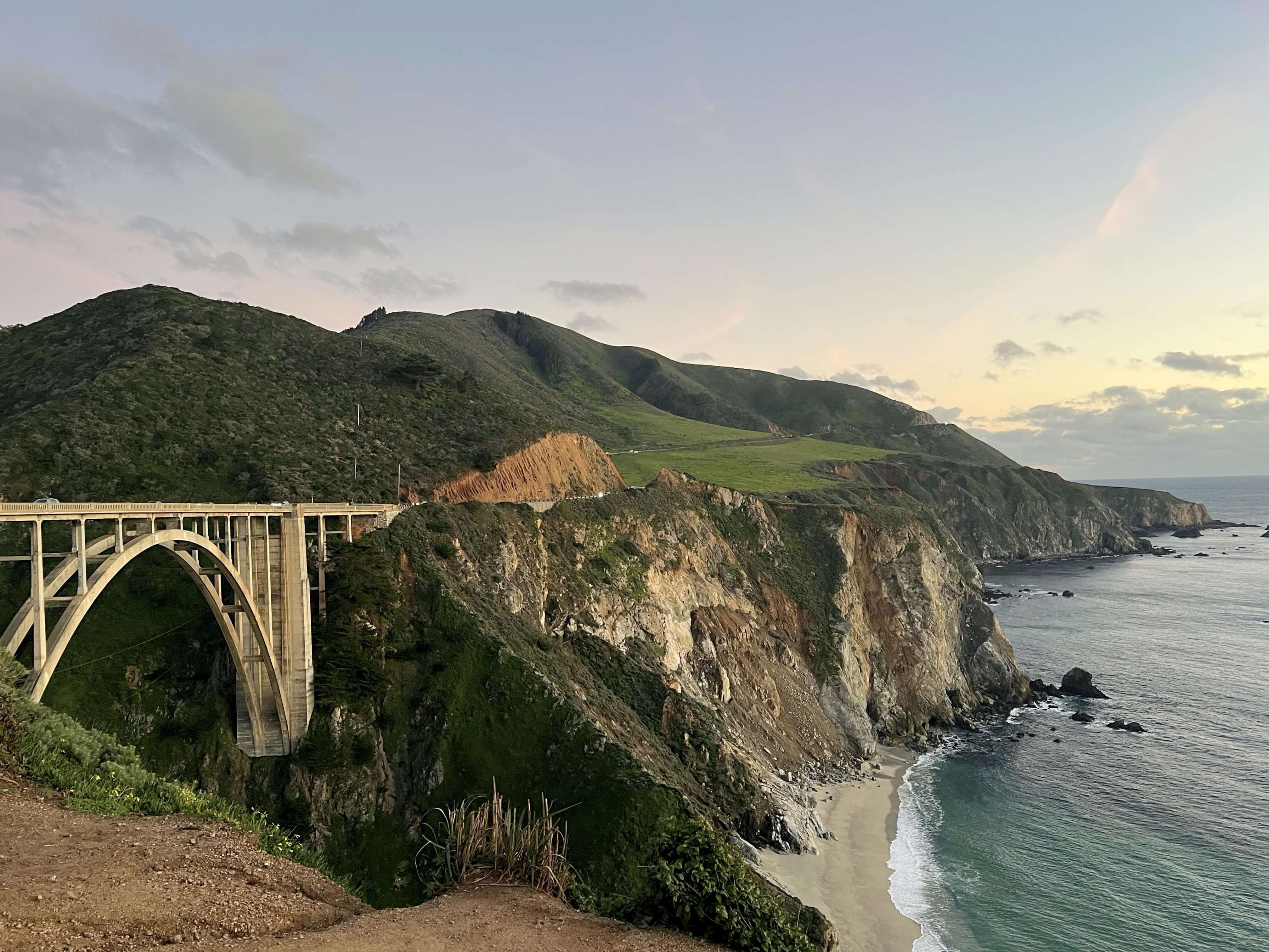 Scenic view of Bixby Creek Bridge along the Big Sur coastline in California, with rugged cliffs and the Pacific Ocean under soft light.
