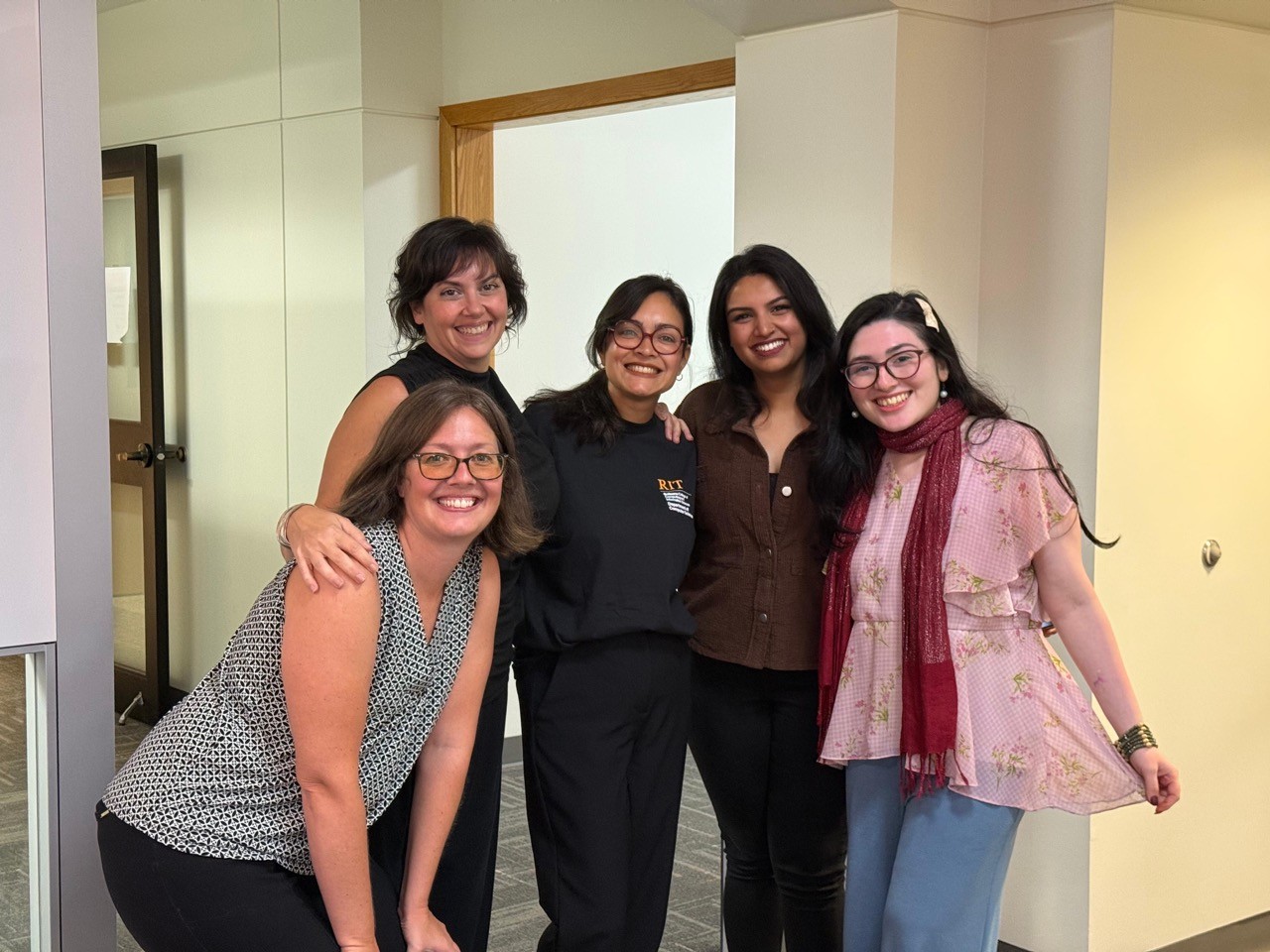 Group of five people smiling and posing together indoors.