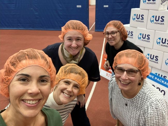 The RIT Graduate School Team in orange hairnets at a meal-packing event