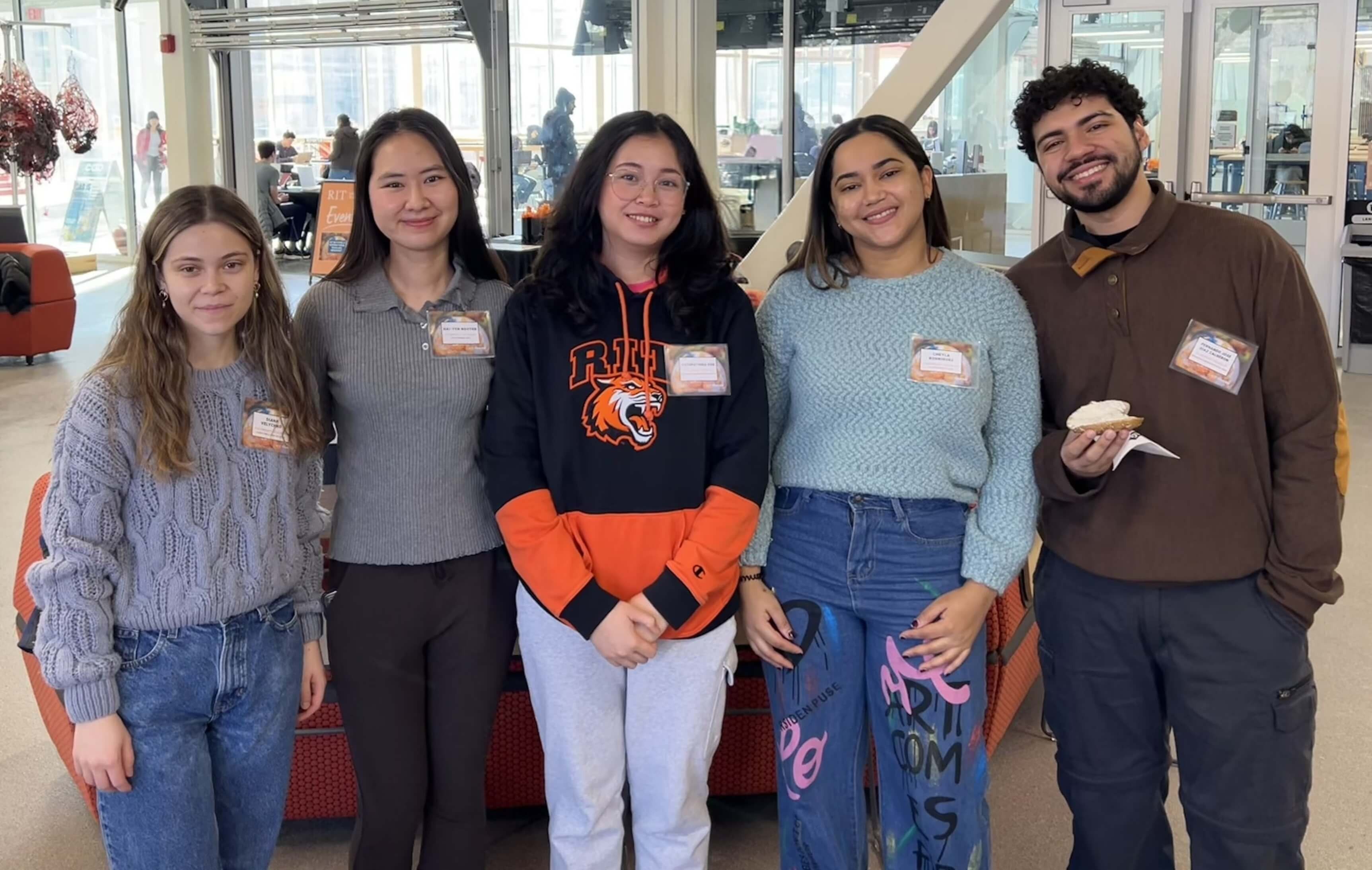 Five young adults stand side by side, smiling at the camera, at the RIT National and International Scholars Breakfast.