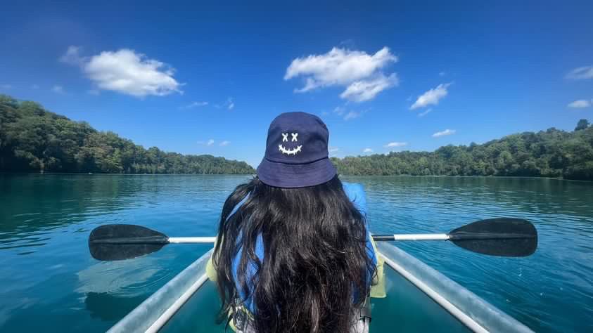 New graduate students sitting on a circular table with one student holding up and showing a gray RIT T-shirt while others smile at the camera