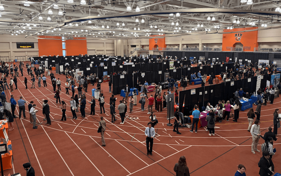 A bustling career fair at RIT, with numerous booths and attendees engaging in discussions, in an indoor setting.