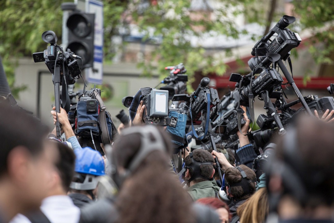 A crowd of journalists holding up cameras and microphones during a media event or press conference.