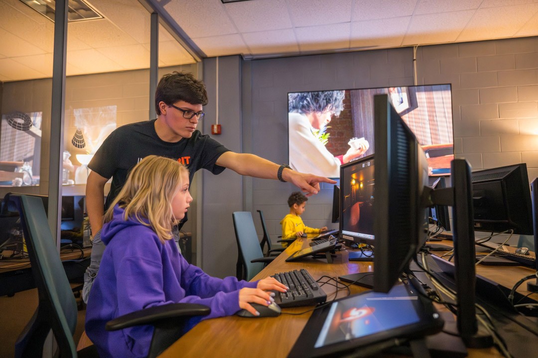 A woman uses a computer in a lab while a man points at her screen.