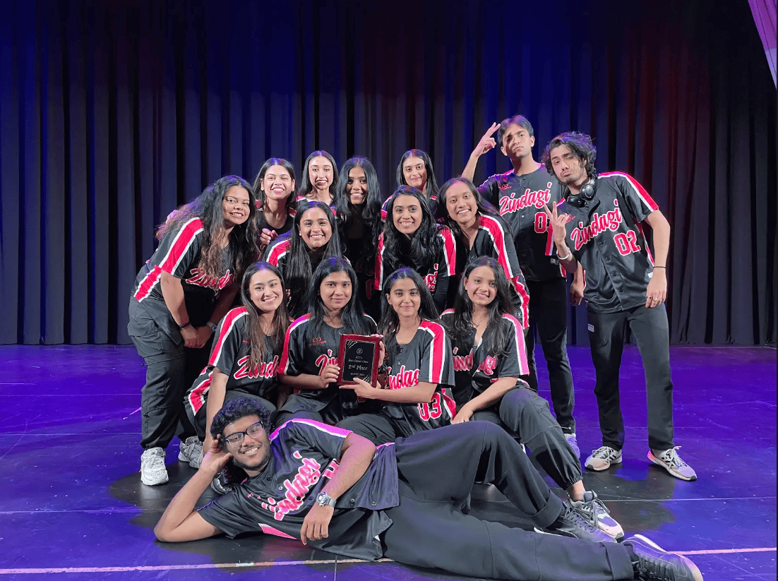 A group of 15 dancers from Zindagi, a dance team at RIT, pose together on stage wearing matching black and red jerseys with "Zindagi" written across the front.