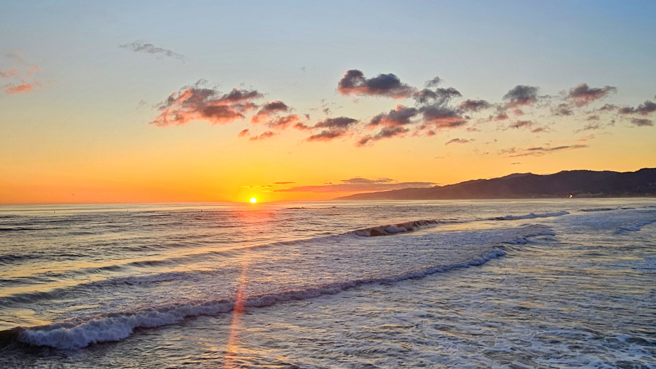 New graduate students sitting on a circular table with one student holding up and showing a gray RIT T-shirt while others smile at the camera