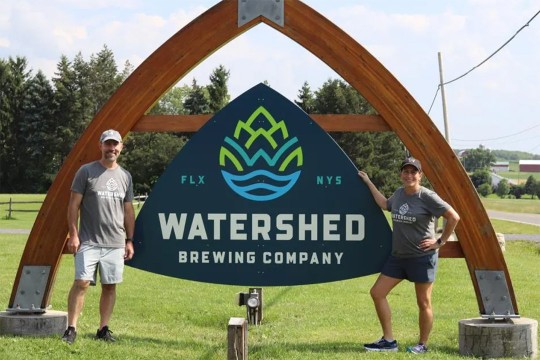 Lisa and Ken Greenwood stand next to the sign for their business Watershed Brewing Company