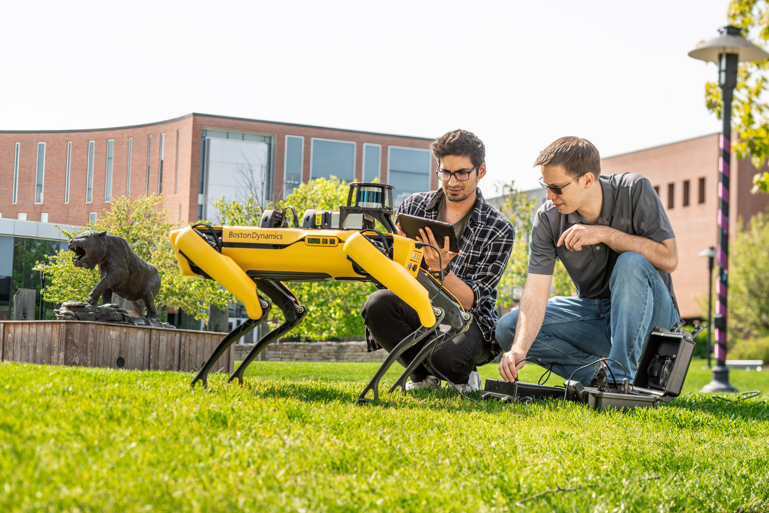 A student and professor crouched down on a lawn looking at a robot dog.