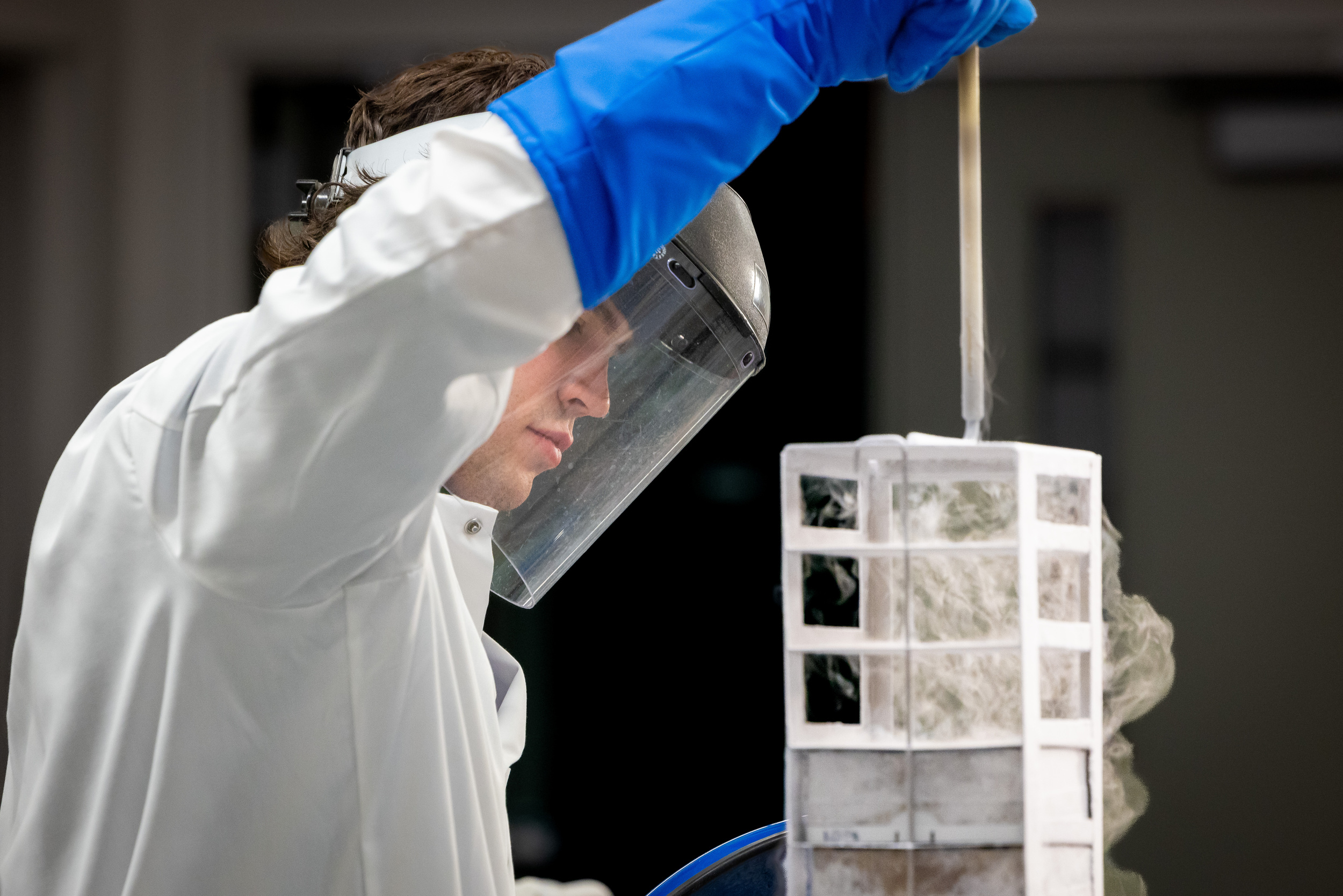 A biomedical engineering graduate student lifting up a device and wearing a face shield.