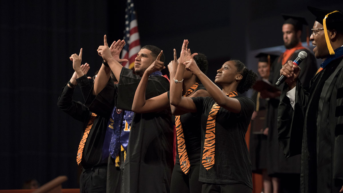 Students perform sign language during a commencement ceremony on stage.