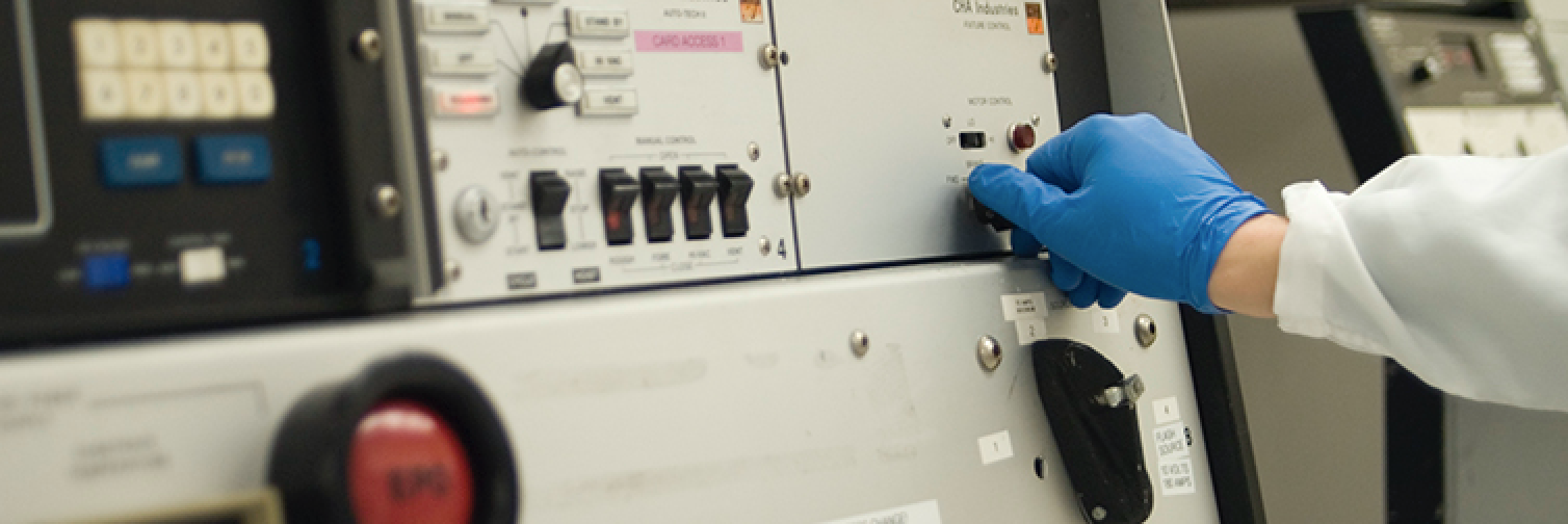 Gloved hand pushing button on lab equipment