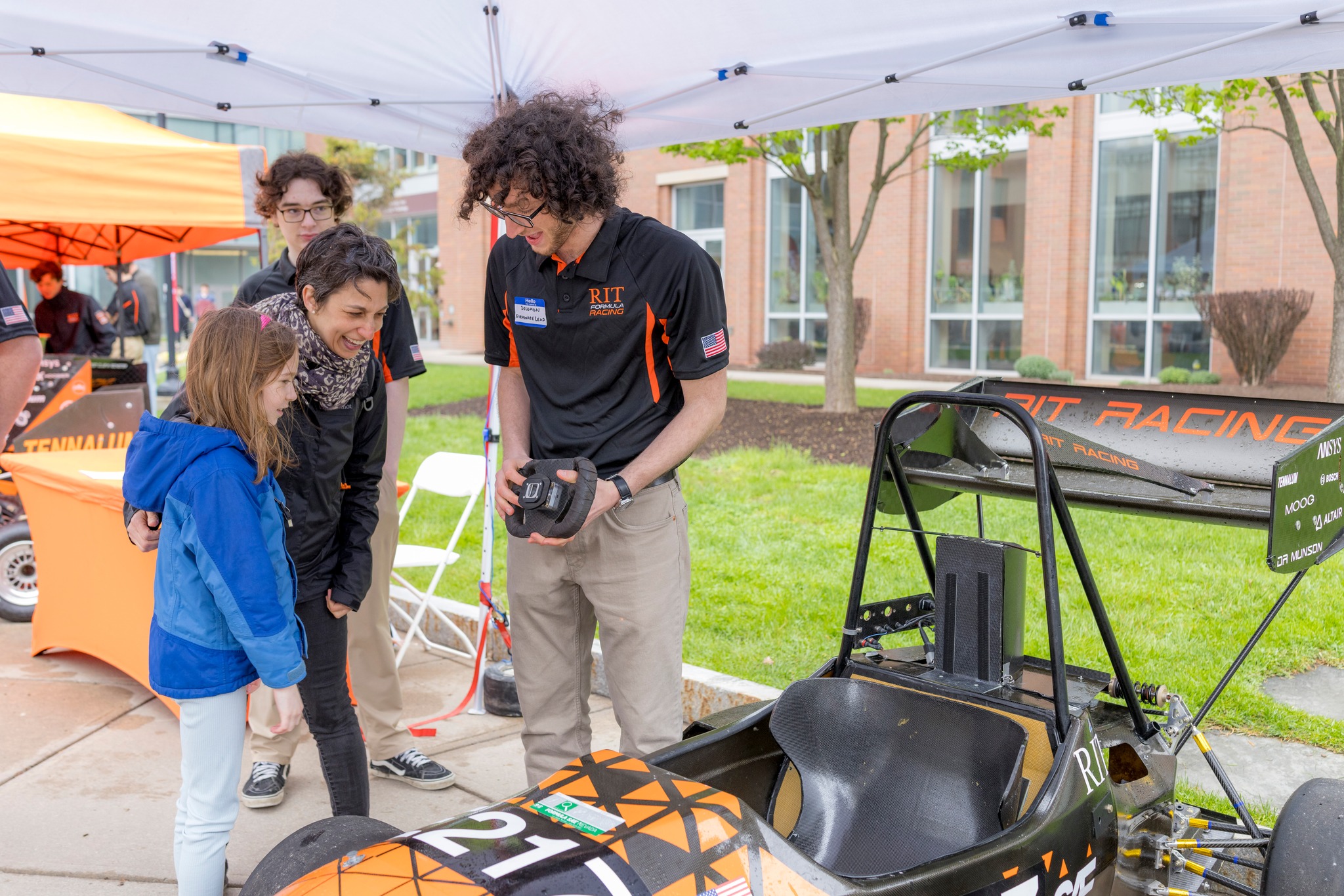 A RIT student talking to two children and standing next to a race car.
