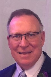A headshot of Peter Arthur wearing a suit and tie and glasses.