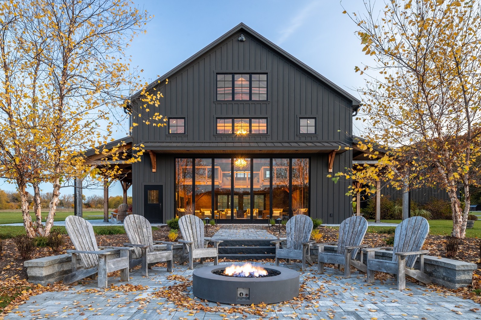 A barn looking structure positioned behind a fire pit surrounded by Adirondack chairs.