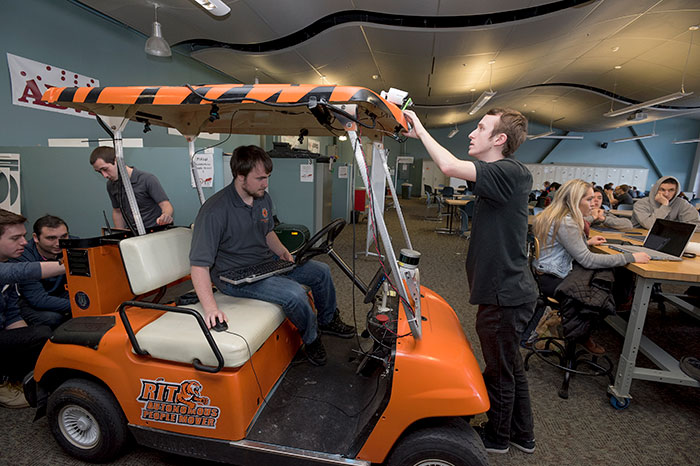 an RIT themed golf cart with students using technology