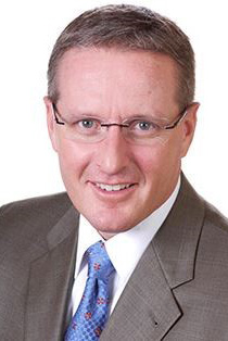 A headshot of Jim Swift wearing a gray suit.