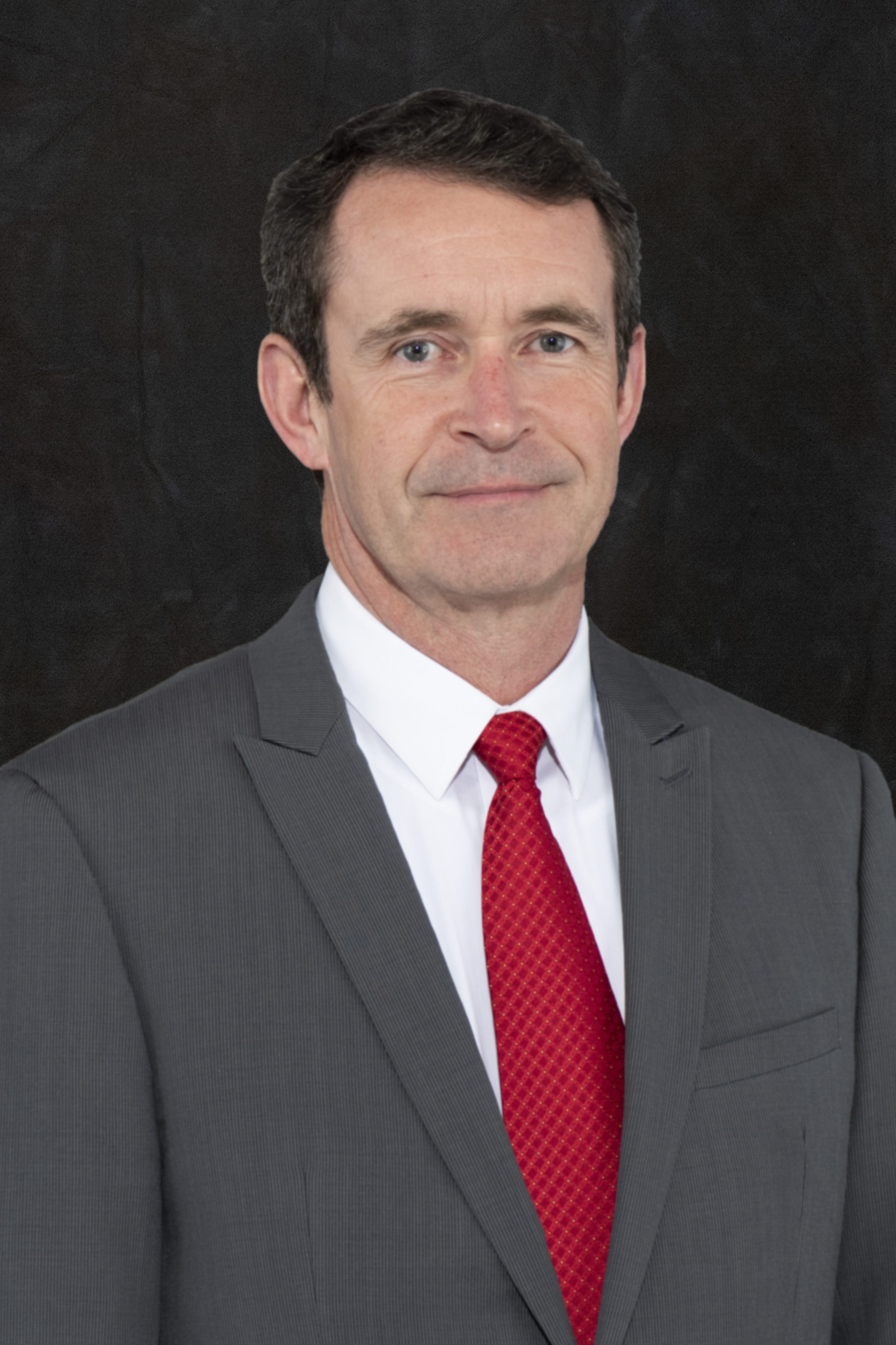 A headshot of Michael Field wearing a gray suit and a red tie.