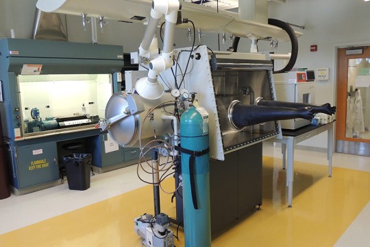 lab with specialized equipment, including a machine with gloves and a large cylindrical container.