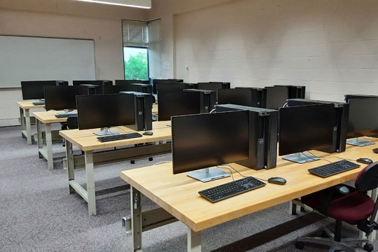 A computer lab with rows of tables with computers and chairs.